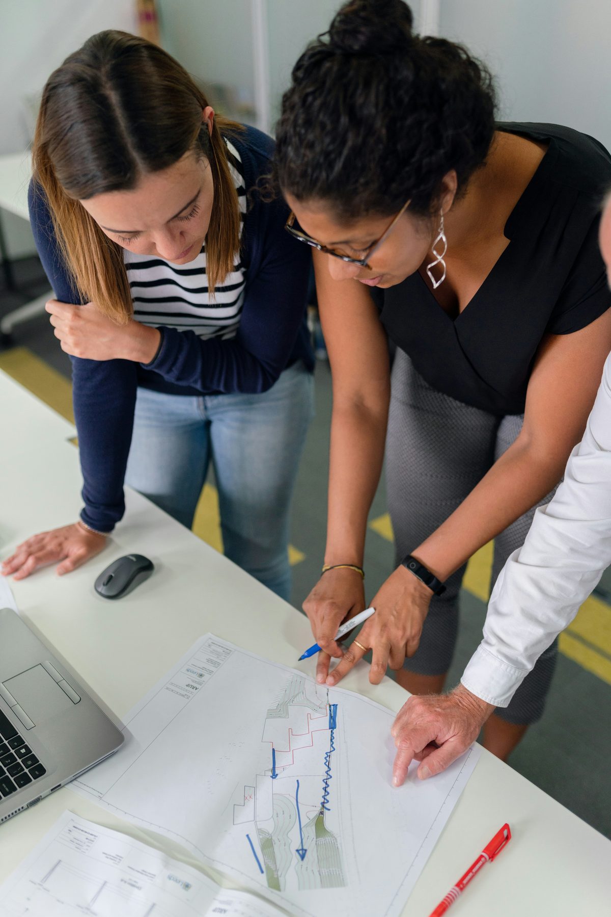 Three colleagues reviewing and annotating a technical drawing together at a desk