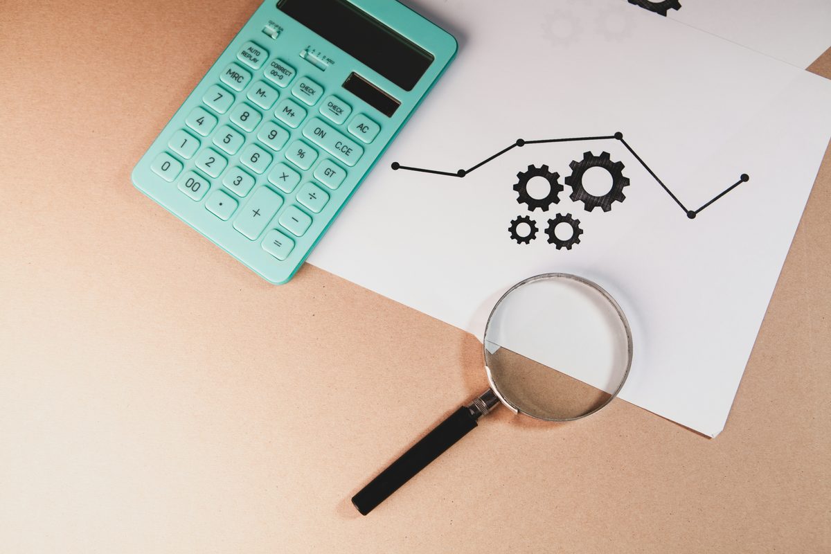 Calculator and magnifying glass next to a hand-drawn process chart with gears